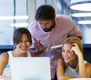 two women and a man looking at a laptop