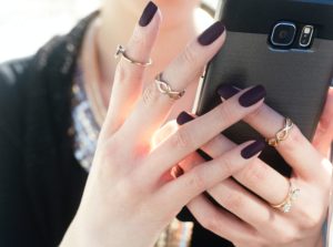 a woman holding up her cell phone with two rings on her fingers