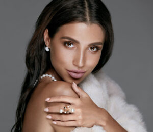 a woman wearing a white fur coat and pearl ring
