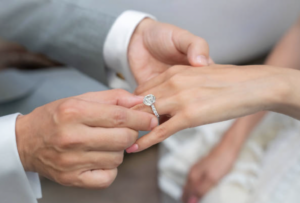 a bride and groom hold hands while putting a ring on their finger