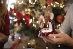 a woman holding a ring in front of a christmas tree